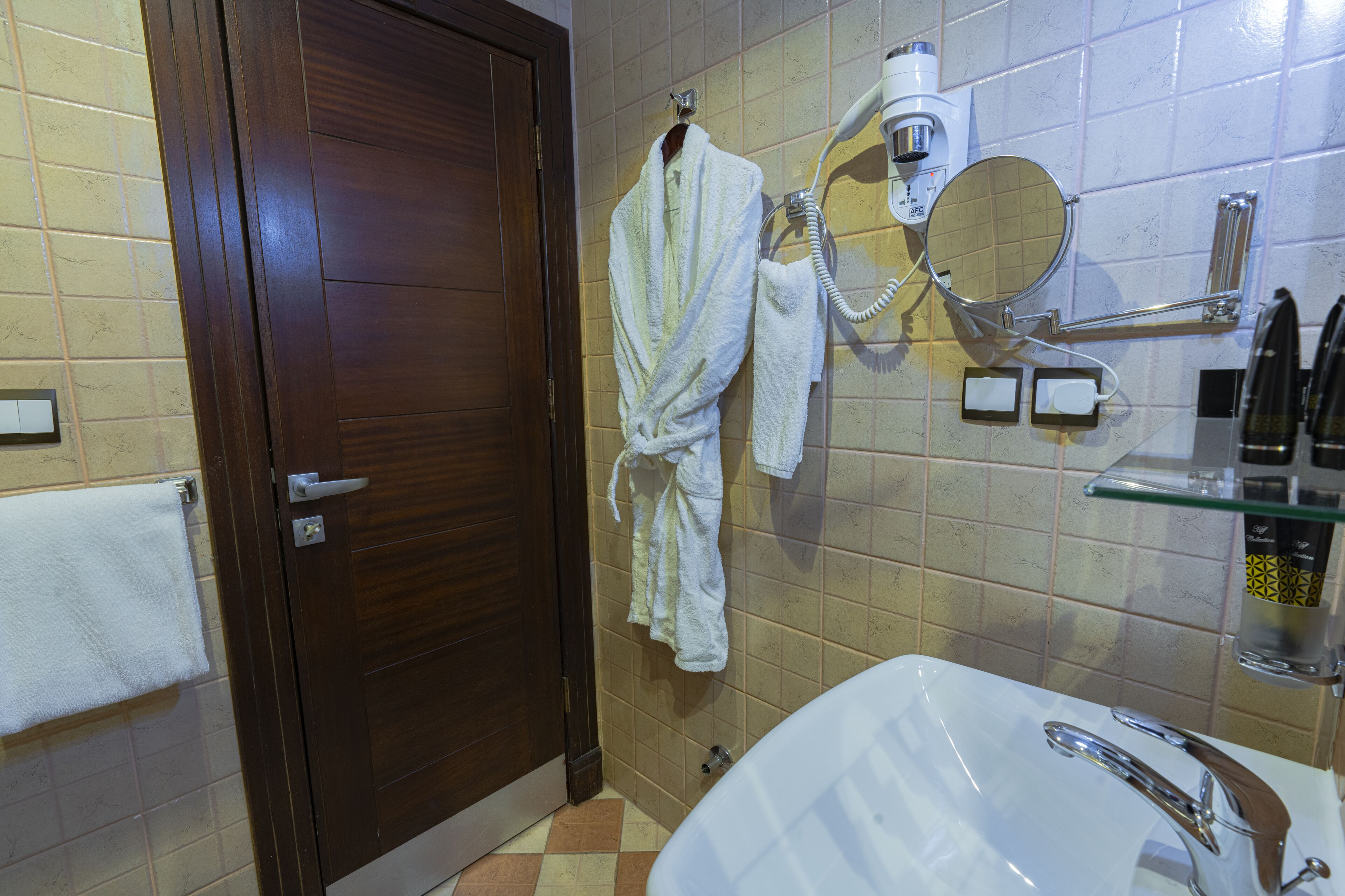 A bathroom with a wooden door, a white sink with a modern faucet, and a towel hanging on the wall.