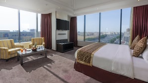 Una habitación de hotel espaciosa con una cama grande, una televisión de pantalla plana, una mesita de café y dos sillones.