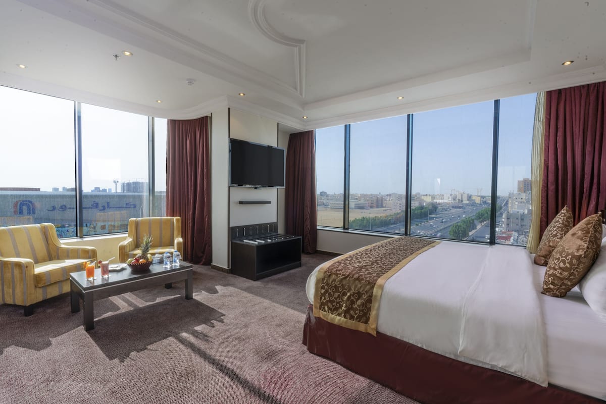 Una habitación de hotel espaciosa con una cama grande, una televisión de pantalla plana, una mesita de café y dos sillones.