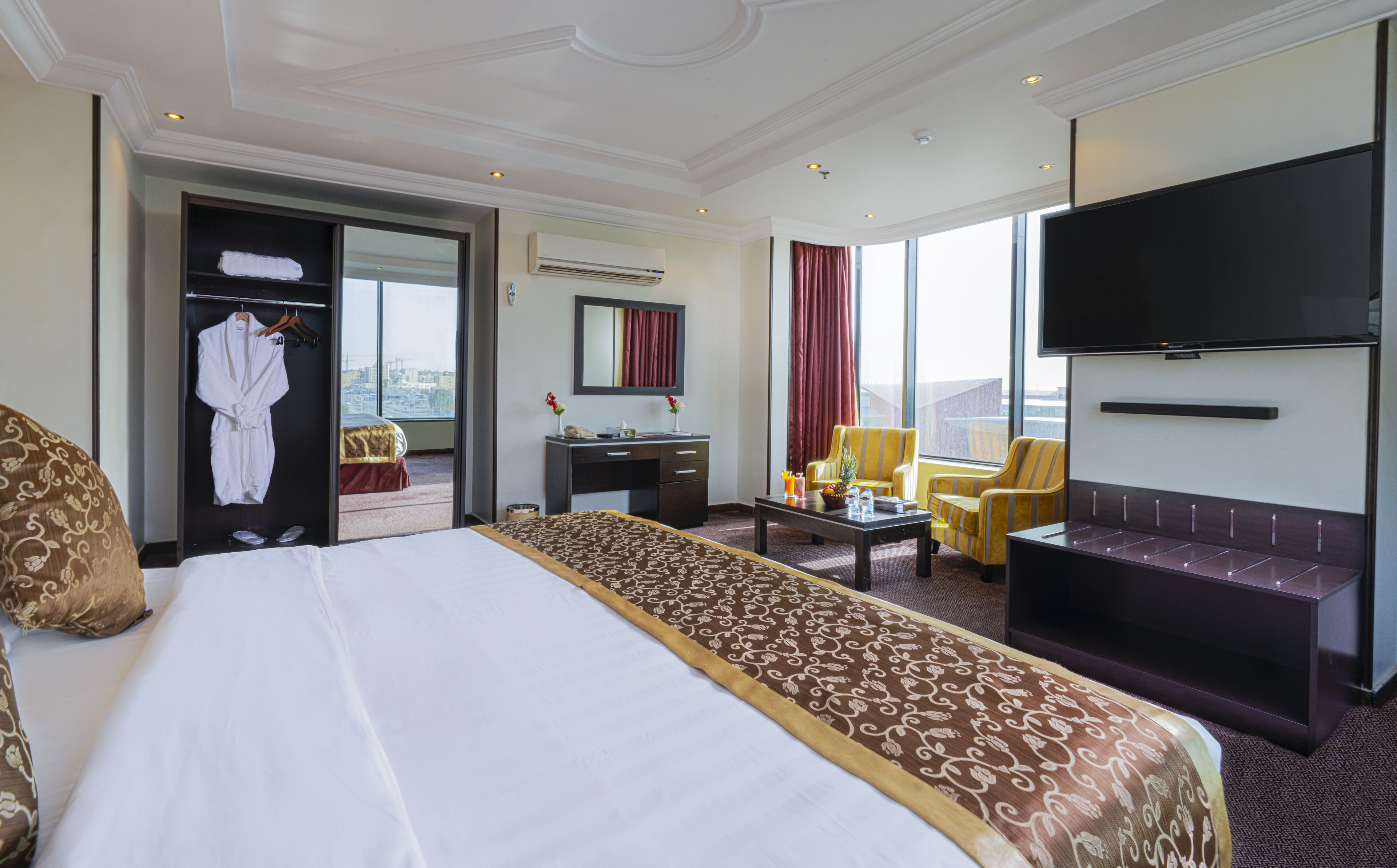 A hotel room with a large bed, a desk, a chair, a sofa, a TV, and a view of the city.