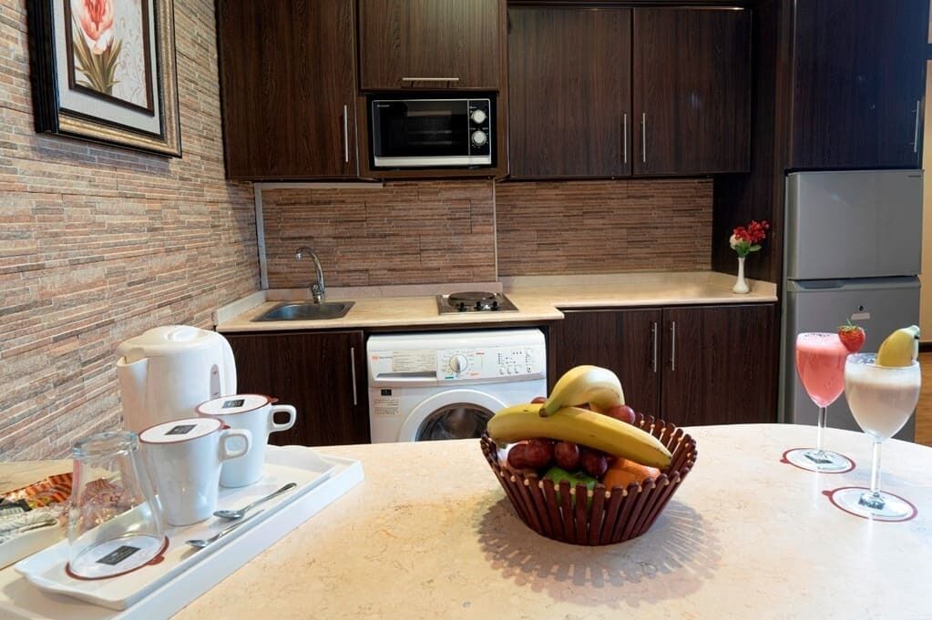 Una cucina moderna con mobili in legno scuro, un forno a microonde, una lavatrice e una ciotola di frutta sul piano di lavoro.