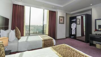 Habitación de hotel con dos camas, un ventanal con cortinas, una bata colgada en la puerta y un escritorio con espejo.