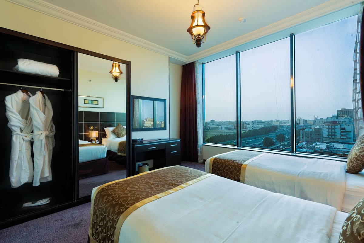 Habitación de hotel con dos camas, un armario, un escritorio y un amplio ventanal con vistas a la ciudad.