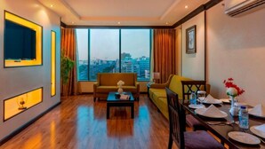 Una habitación de hotel moderna con un ventanal grande, un sofá, una mesa de comedor y un televisor fijado a la pared.