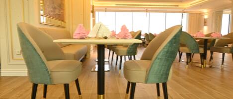 A dining area with round tables and chairs, a chandelier, and large windows.