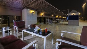 Un área con mesas y sillas para disfrutar al aire libre, una sección techada y un edificio al fondo.