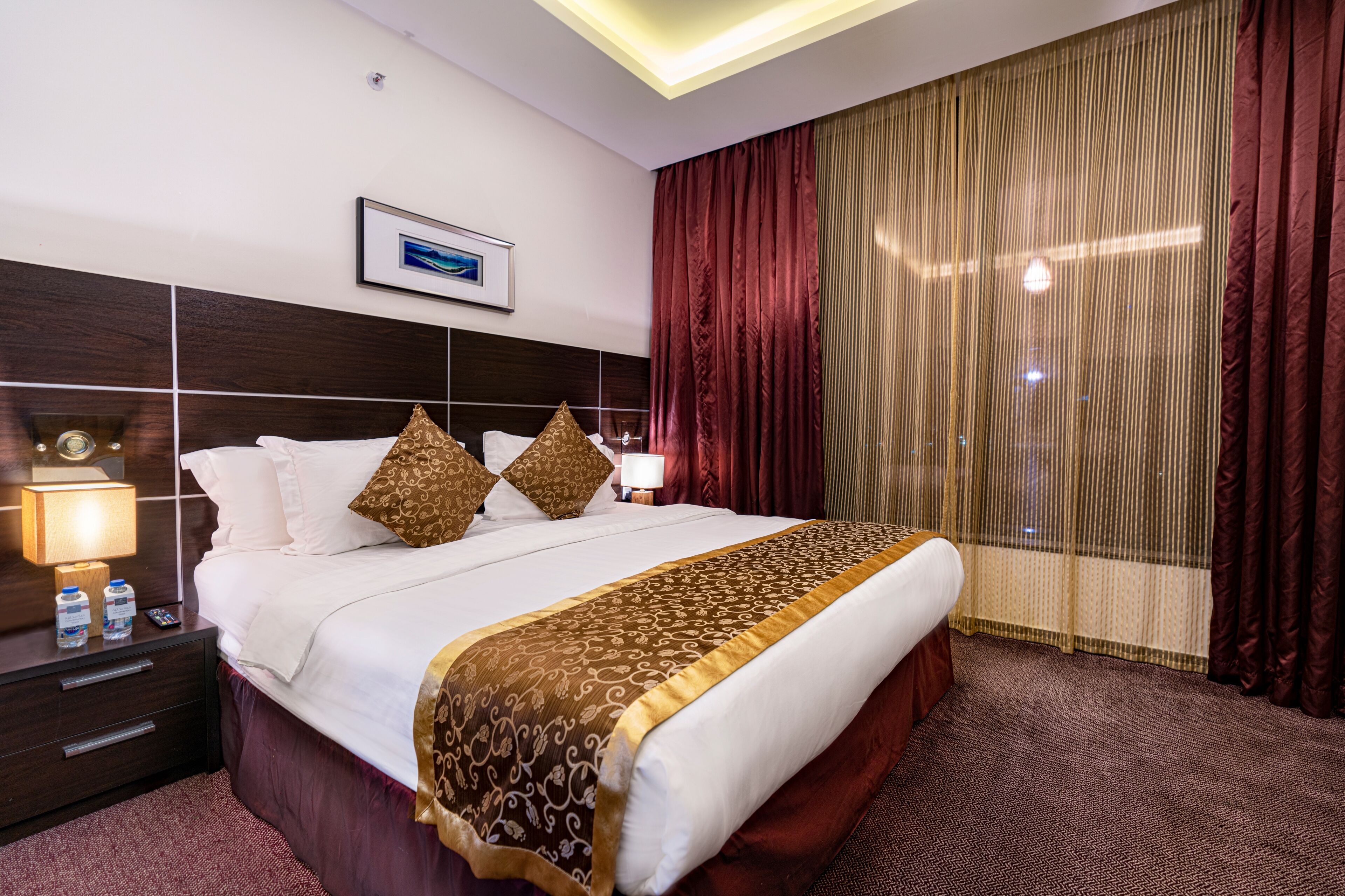 A hotel room with a large bed, a nightstand with a lamp, and a window with curtains.