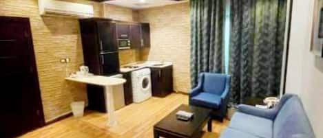 A modern living room with wooden flooring, a sofa, a coffee table, and a kitchen area with a washing machine.