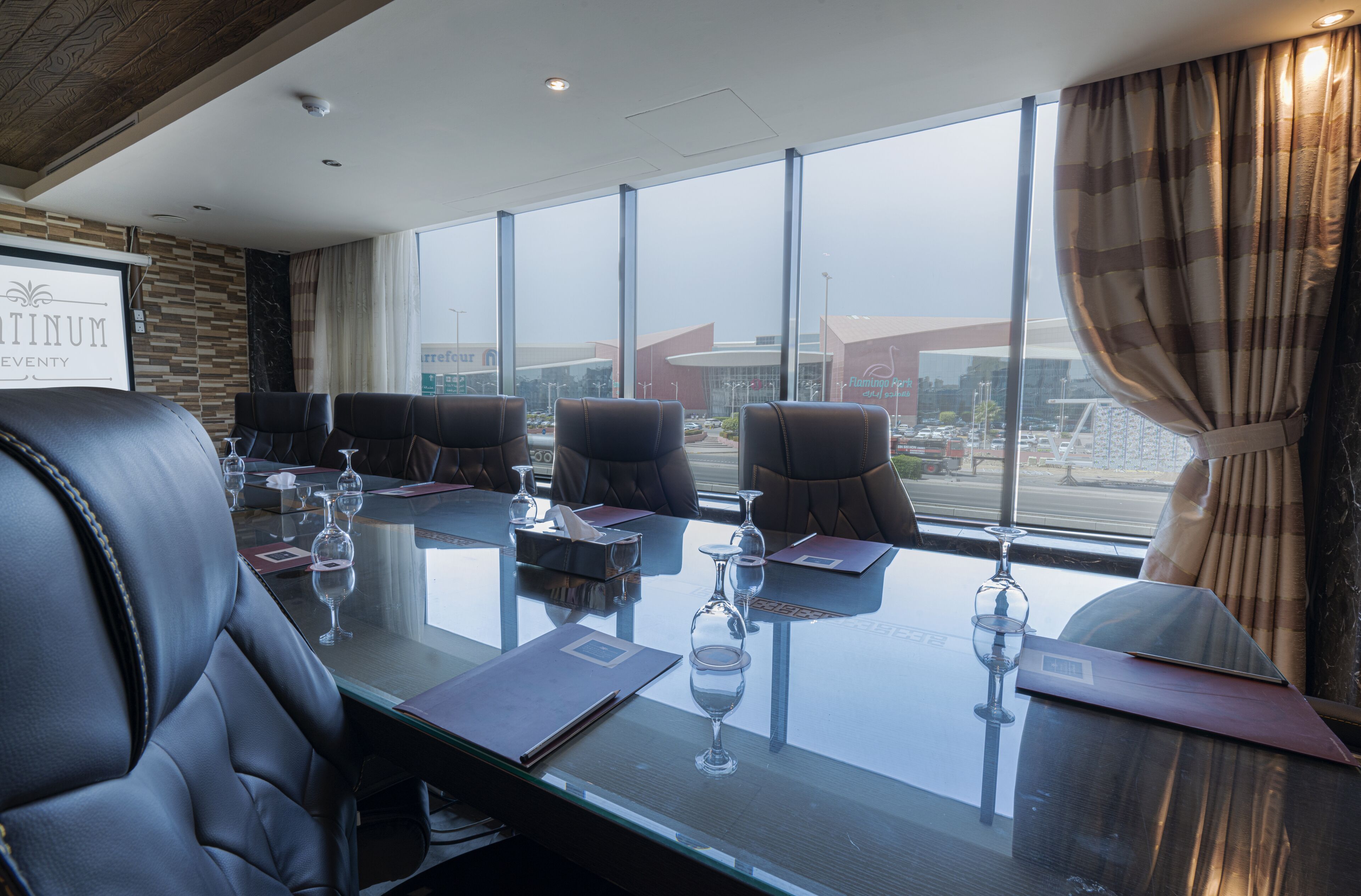 A conference room with a glass table, leather chairs, and a view of a cityscape through large windows.