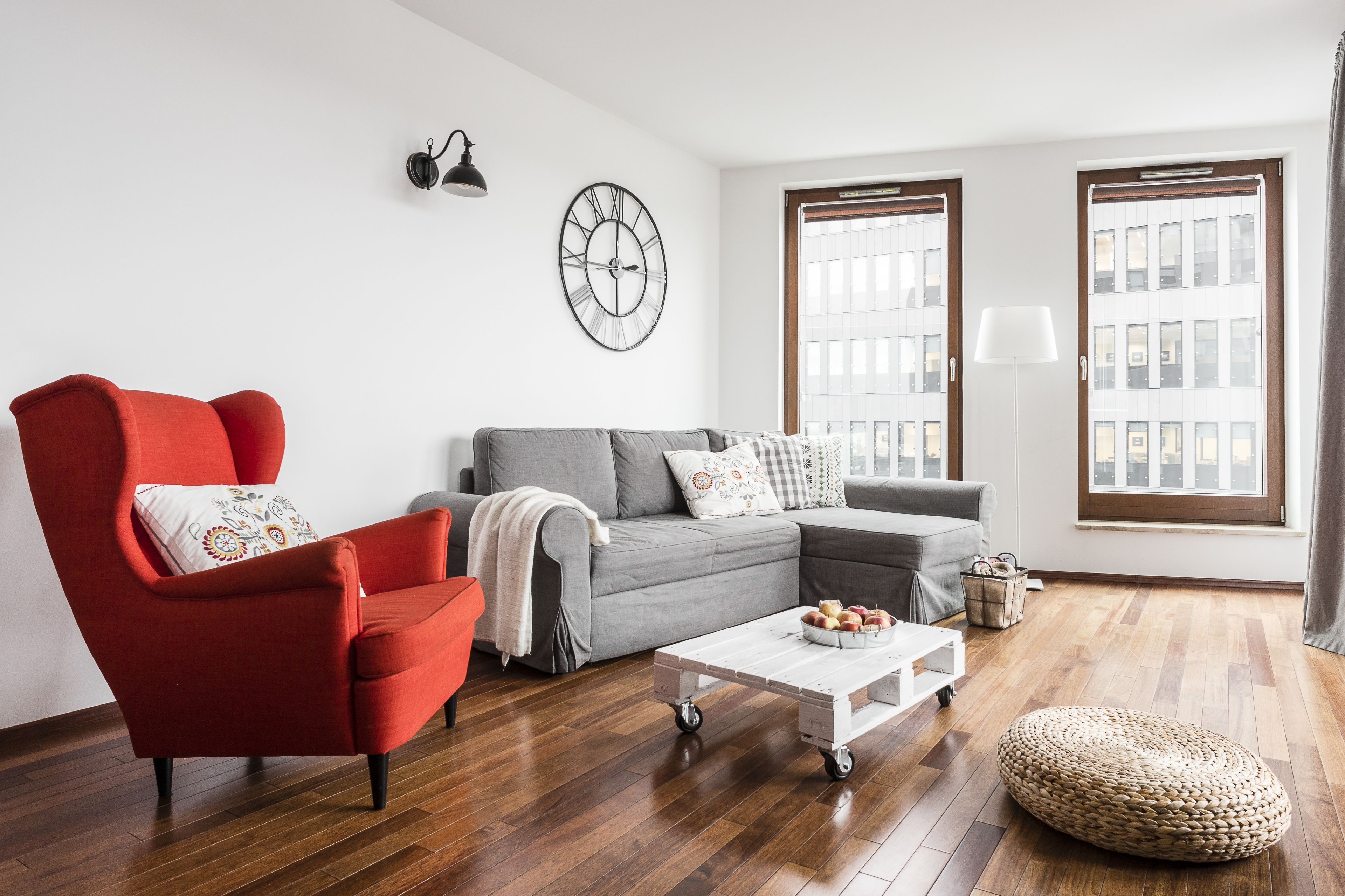 Una sala de estar moderna con un sillón rojo, un sofá gris y una mesa de centro blanca con frutas.