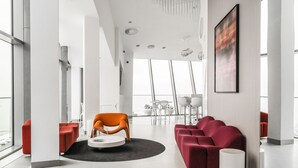 Un intérieur moderne avec un canapé rouge, un fauteuil orange et une table blanche, dans un espace lumineux et ouvert doté de grandes fenêtres.