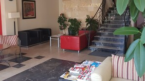 A lobby with a red sofa, a white sofa, a marble floor, a staircase, and a wall with a nameplate.