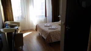 A hotel room with a bed, a chair, a table with a water bottle, and a lamp.