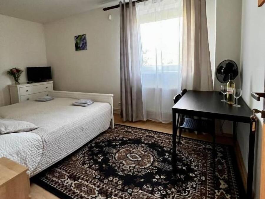 Ein Schlafzimmer mit Bett, Schreibtisch, Stuhl, Teppich und einem Fenster mit Vorhängen.