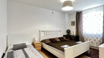 Un dormitorio con una cama individual, una cama más pequeña, una mesita de noche, una lámpara, un aparador, un espejo y una ventana con cortinas.