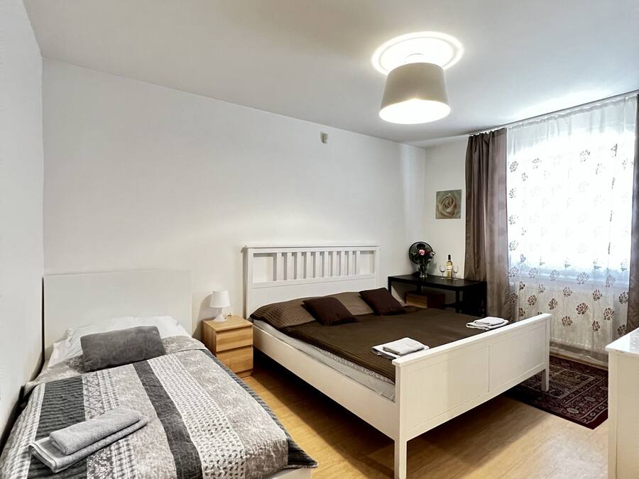 Un dormitorio con una cama individual, una cama más pequeña, una mesita de noche, una lámpara, un aparador, un espejo y una ventana con cortinas.