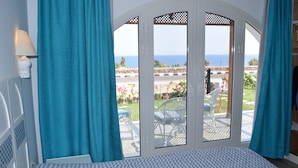 A room with a bed, a view of the sea through a glass door, and a patio with chairs and flowers. - Domina Coral Bay Vacation House (Sharm El Sheikh)
