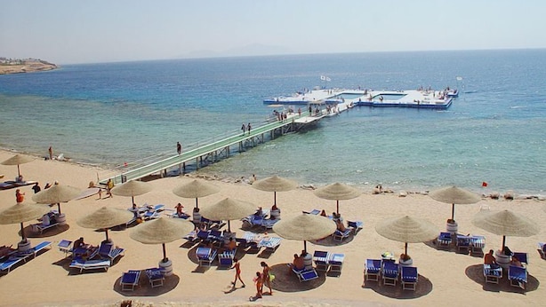 A beach with sun loungers and umbrellas, a pier extending into the sea, and boats docked. - Domina Coral Bay Vacation House (Sharm El Sheikh)