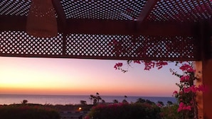 A covered outdoor area with a view of the sea at sunset, a gate, and some flowering plants. - Domina Coral Bay Vacation House (Sharm El Sheikh)