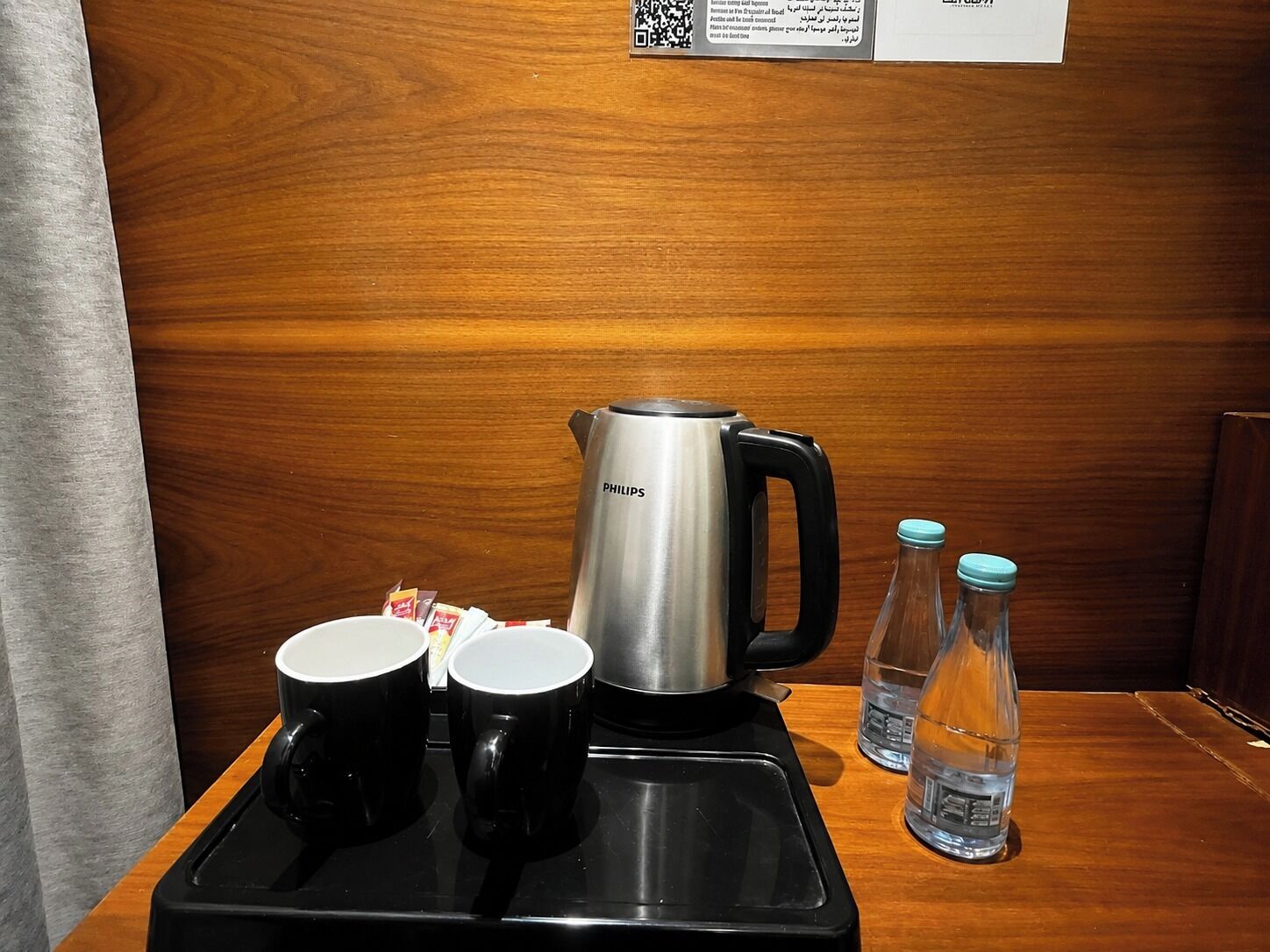 A tray with a coffee maker, two black mugs, and two water bottles on a wooden table.