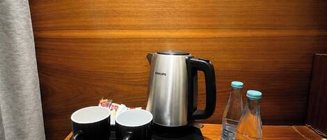 A tray with a coffee maker, two black mugs, and two water bottles on a wooden table.