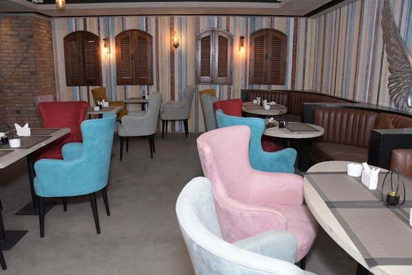 A restaurant interior with striped wallpaper, wooden shutters, and a variety of seating including chairs and a booth.