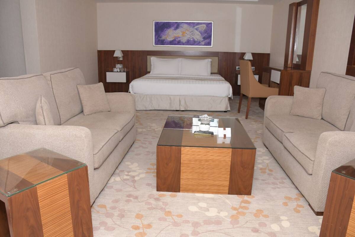 A hotel room with a bed, two sofas, a coffee table, and a painting on the wall.