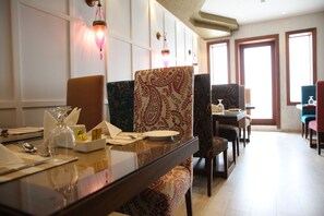 A dining area with patterned chairs, a table set for two, and decorative wall sconces. - Palm Boutique Hotel (Jeddah)