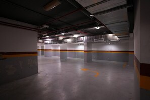 Sisätiloissa sijaitseva pysäköintihalli, jossa on betonipilarit, keltaiset opasteet ja ylhäältä tuleva valaistus.