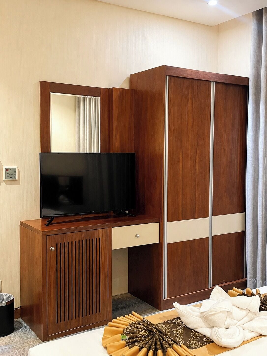 Camera d'albergo con una scrivania in legno, una televisione, un armadio e un letto con una coperta ben sistemata.