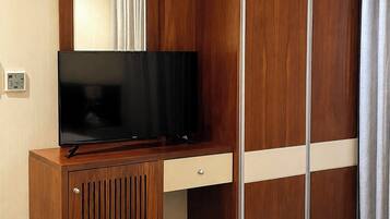 Camera d'albergo con una scrivania in legno, una televisione, un armadio e un letto con una coperta ben sistemata.