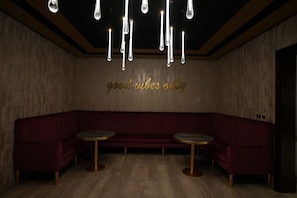 A dimly lit room with a red upholstered bench and two small round tables. - Palm Boutique Hotel (Jeddah)