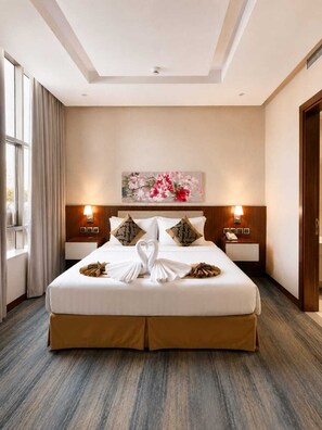 A hotel room with a large bed, two bedside tables with lamps, a painting above the bed, and a window with curtains. - Palm Boutique Hotel (Jeddah)