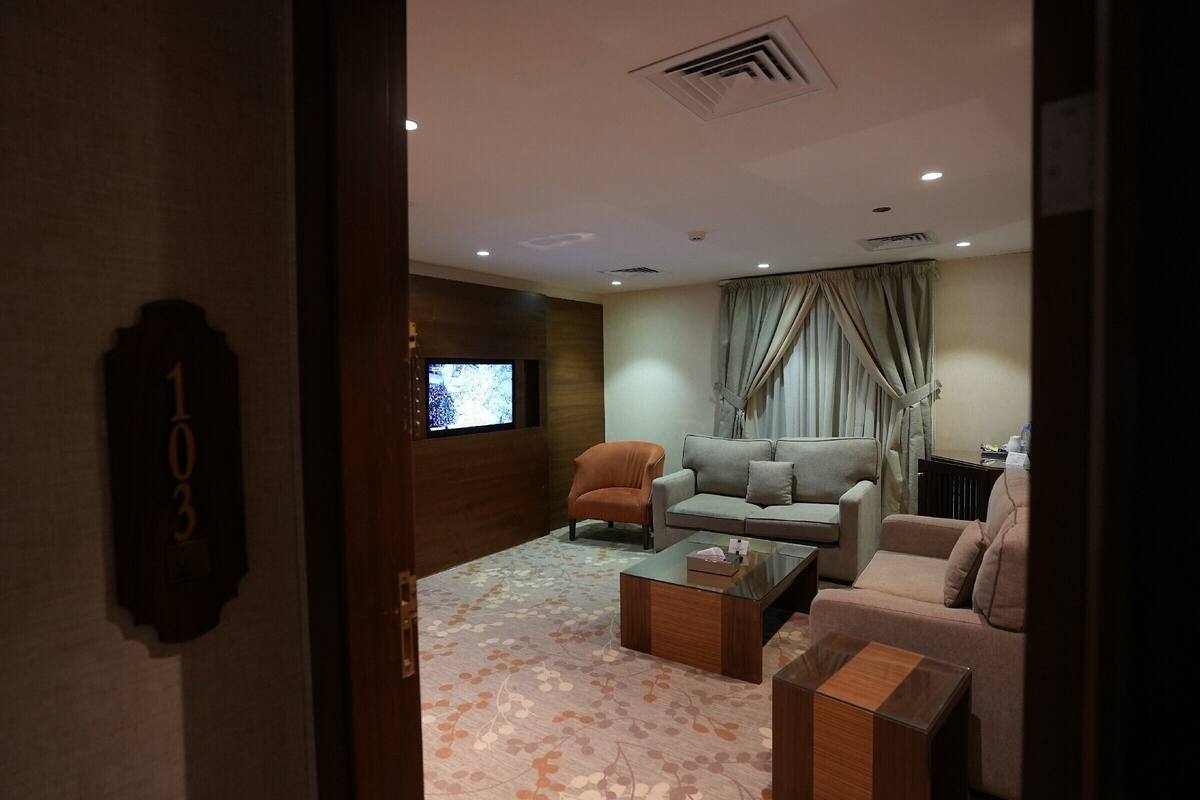 A modern living room with a sofa, armchair, and coffee table. A television is mounted on the wall, and curtains are drawn over a window.