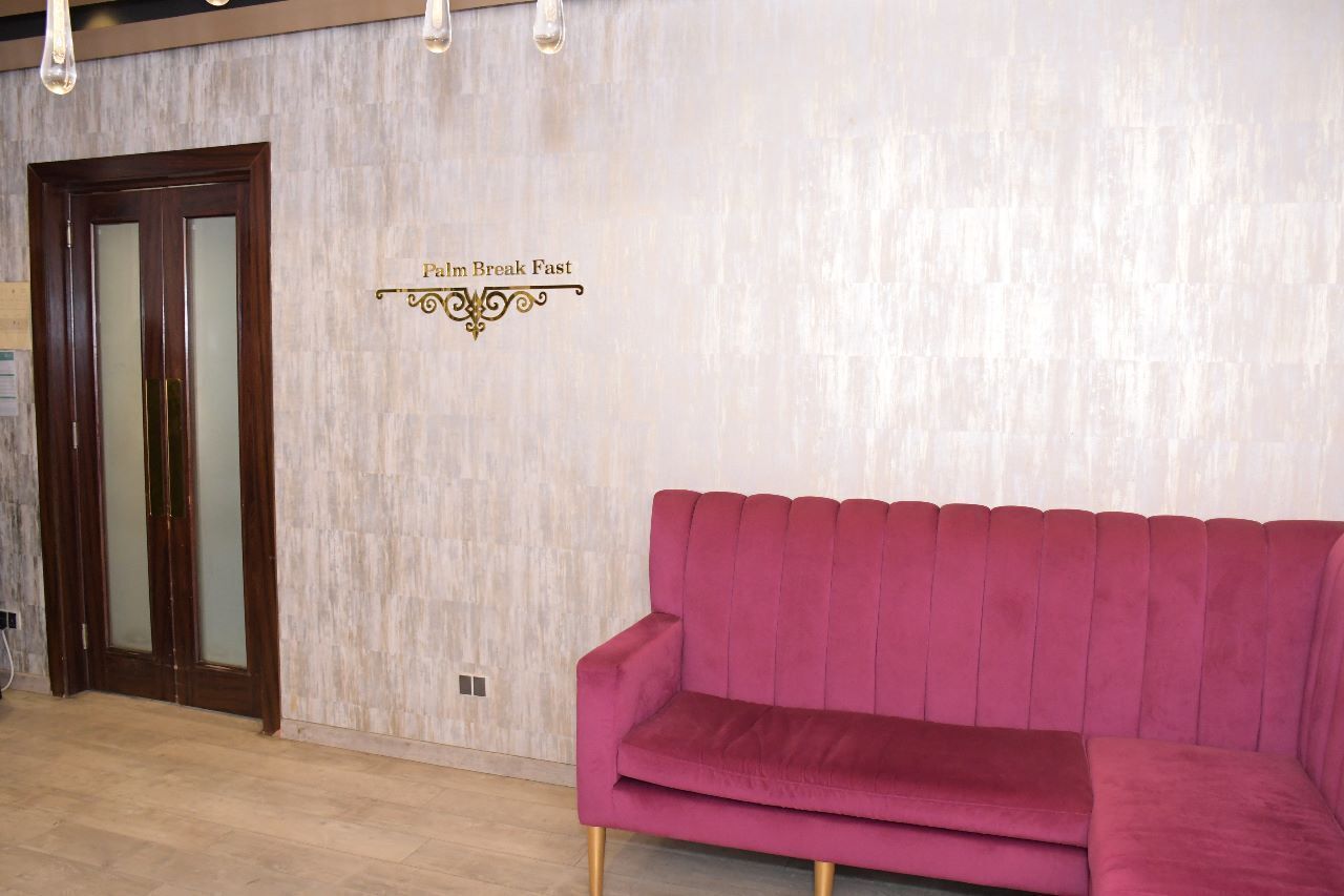 A reception area with a wooden door and a sign that reads "Palm Break Fast." A pink sofa is positioned in front of the door.