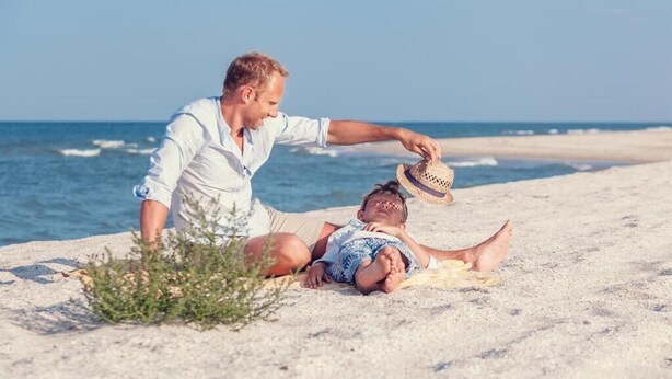 A person sitting on a beach towel, another person lying on the sand, and a hat on the ground. - Haffnera 19 - Sea & City Moments by Lion Apartments Sopot (Sopot)