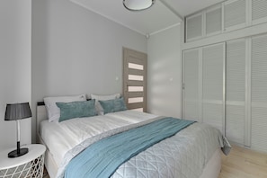 A bedroom with a bed, bedside table, lamp, and a closet with louvered doors. - Lion Apartments - Haffnera 19 (Sopot)