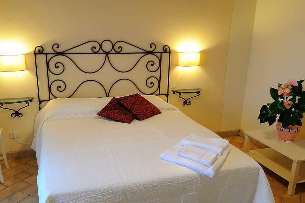 A neatly made bed with a decorative headboard, two bedside lamps, a small table with a plant, and a chair.