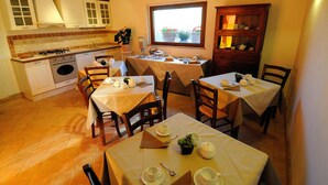 A dining area with tables set for tea service, a kitchen with a gas stove, and a view through a window. - Cerchio Verde (Pitigliano)