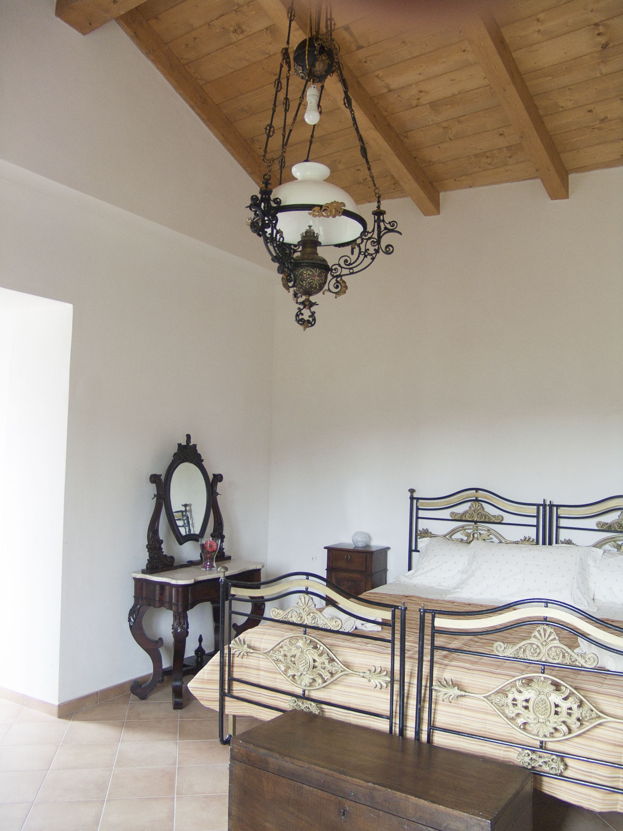 A bedroom with a wooden ceiling, a bed with ornate metal headboard, a wooden dresser, and a mirror.