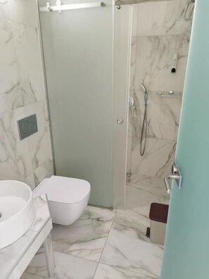 Une salle de bain dotée d’une douche à parois de verre, de toilettes blanches et d’un sol carrelé en marbre.