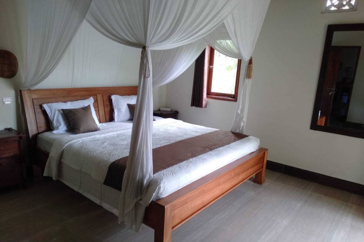 Ein geräumiges Schlafzimmer mit einem großen Bett, einem Holzkopfende und einem Baldachin.