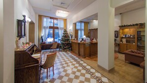 A spacious living area with a checkered floor, a wooden dining set, a Christmas tree, and a kitchen area with a wooden cabinet and a refrigerator. - Capsis Bristol Boutique Hotel (Thessaloniki)