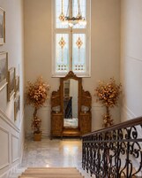 A grand staircase with a wrought iron railing, a large mirror, and two potted plants with autumn leaves.