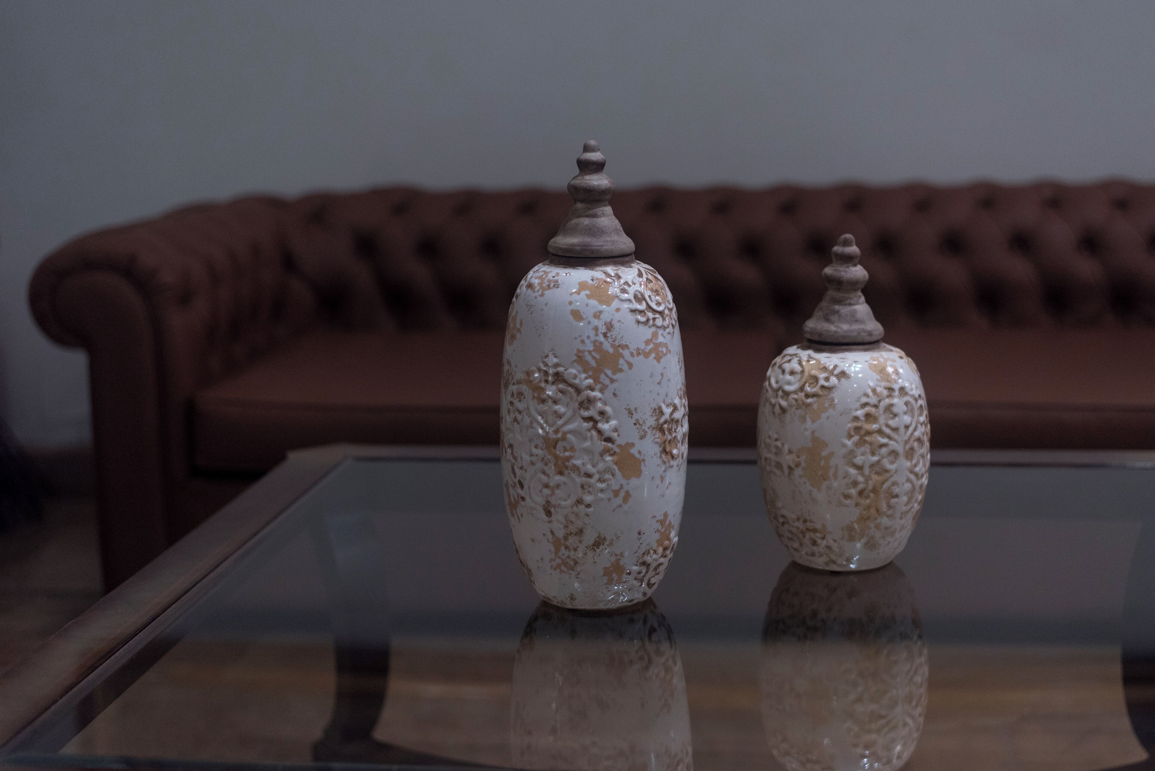 Two ceramic vases on a glass table with a brown sofa in the background.