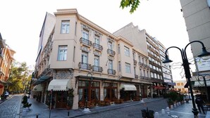 A multi-story building with a cafe on the ground floor, featuring outdoor seating and a cobblestone street. - Capsis Bristol Boutique Hotel (Thessaloniki)