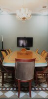 Un'area pranzo con un grande tavolo ovale, sedie, un lampadario, un televisore a schermo piatto e una ventola da terra.
