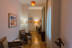 Una habitación de hotel con piso de madera, un escritorio, una silla, una lámpara y un cuadro en la pared.