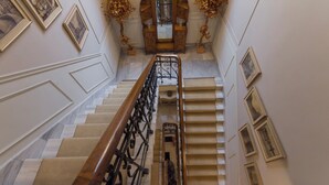 A grand staircase with a wooden handrail, marble steps, and framed pictures on the walls. - Capsis Bristol Boutique Hotel (Thessaloniki)