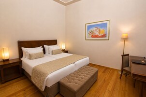 Habitación de hotel con una cama grande, lámparas de noche, un escritorio y un cuadro en la pared.